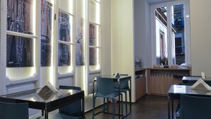 Un espace repas moderne avec des tables et des chaises en verre, un comptoir de cuisine et de grandes fenêtres ornées d’œuvres d’art.