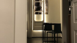 Un couloir avec une porte donnant sur une pièce, une petite table avec deux chaises et un luminaire fixé au mur.