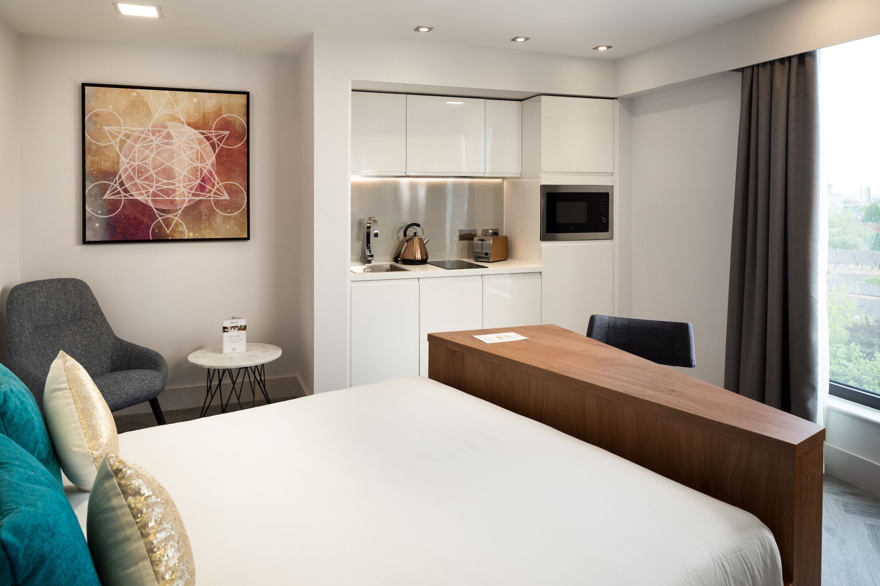 Une chambre d’hôtel équipée d’un lit, d’un bureau, d’une chaise, d’une petite table, d’une bouilloire, d’un grille-pain et d’un téléviseur.
