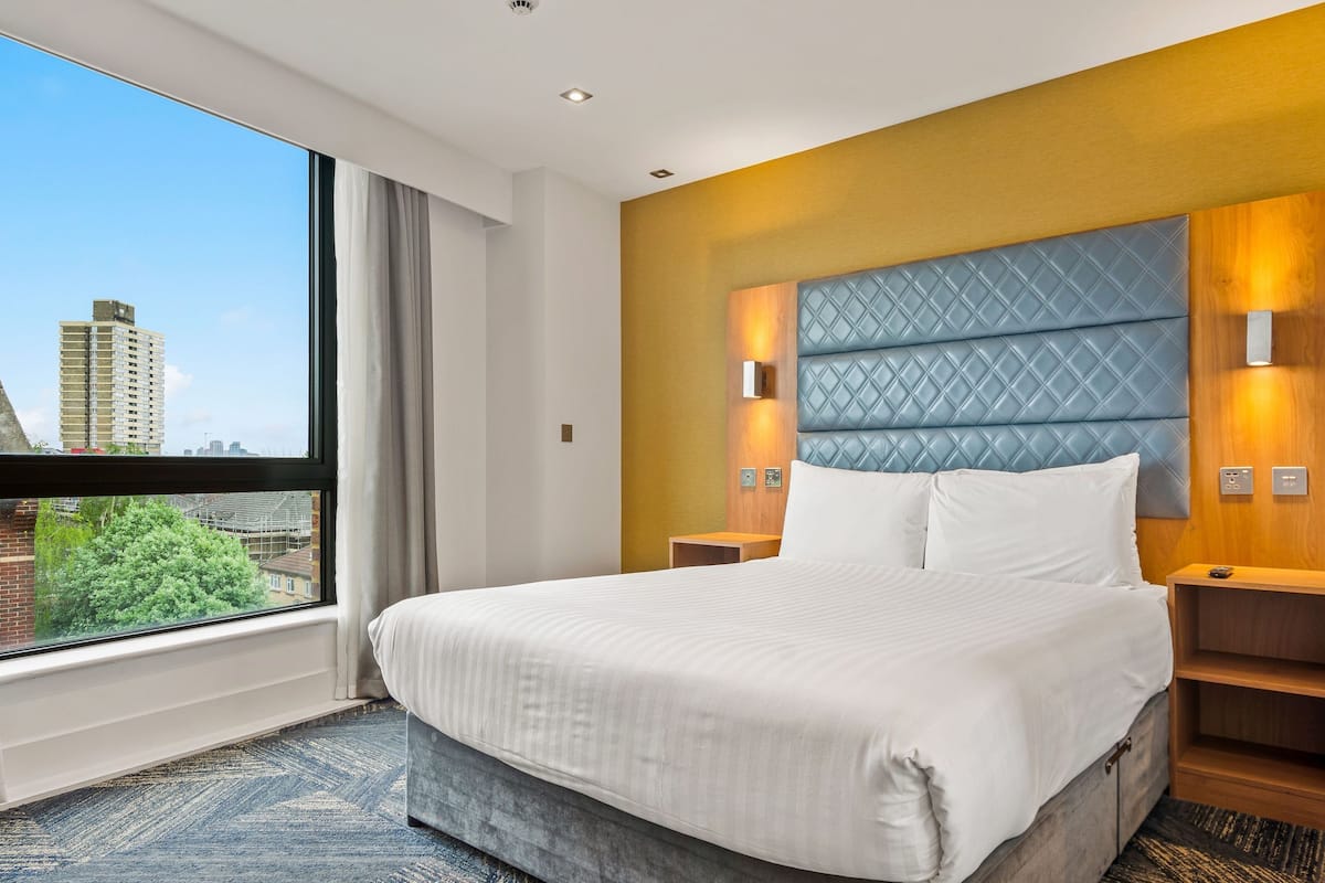 A hotel room with a large bed, a view of the city, and a modern headboard.