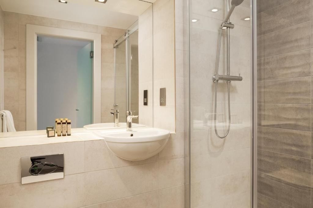 A modern bathroom with a glass-enclosed shower, a white sink, and a mirror.