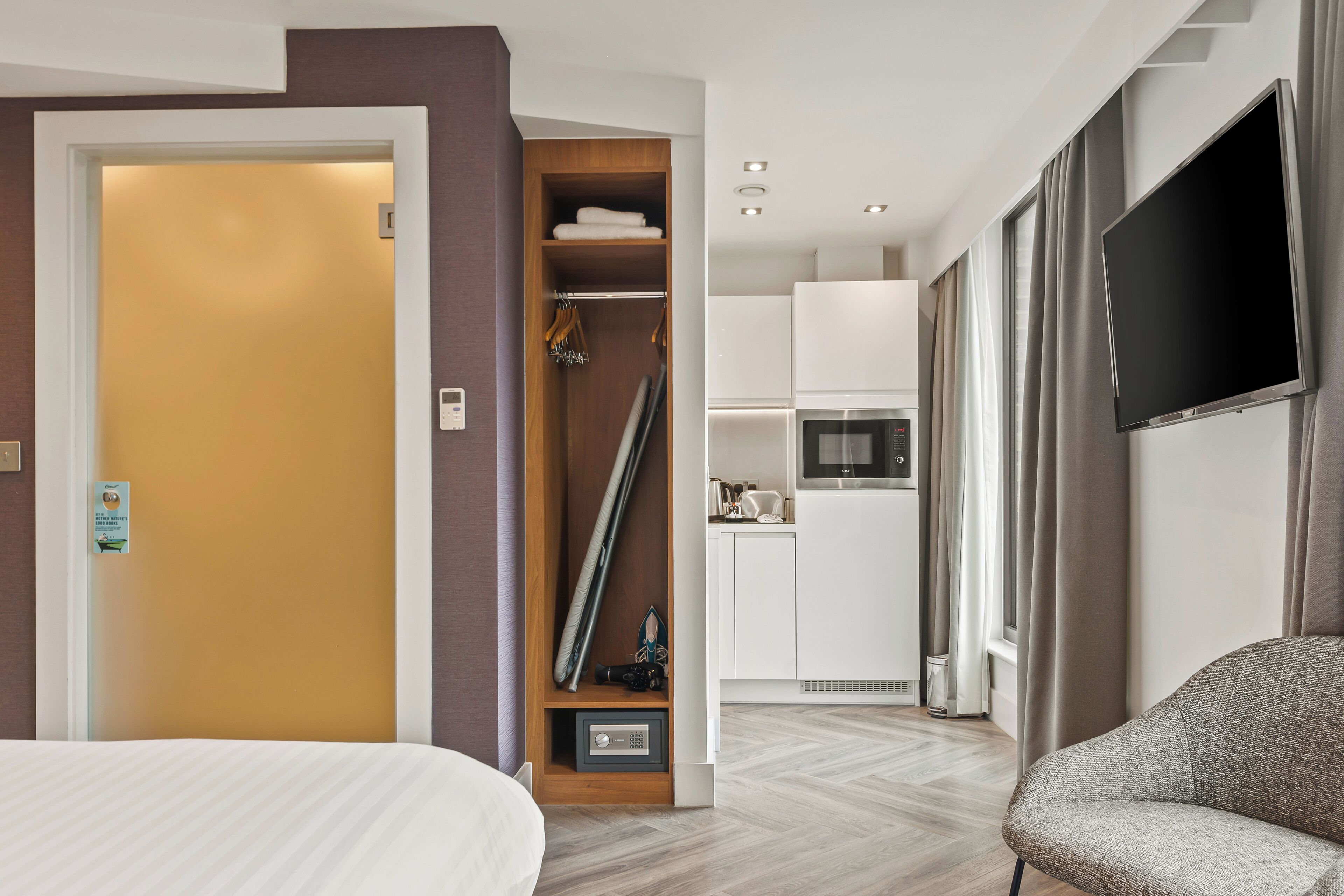 Una habitación de hotel con cama, armario, televisor y kitchenette.