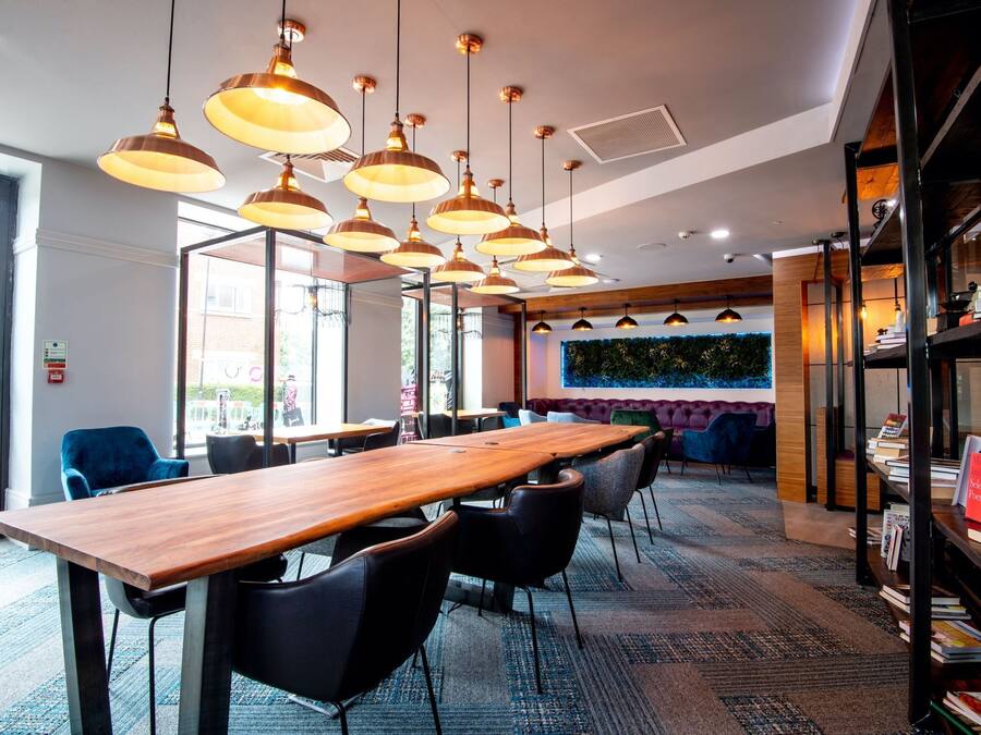 A modern conference room with a long wooden table, black chairs, and multiple pendant lights.