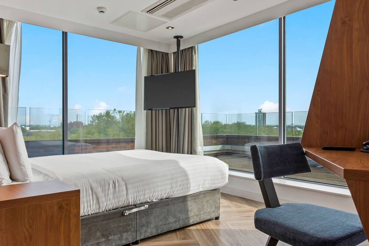 A modern hotel room with a large bed, a desk, and a TV.
