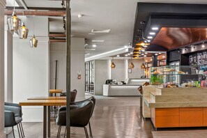 A modern cafe interior with a reception desk, seating area, and a display case with pastries.