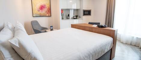 Camera d'albergo con un letto grande, una scrivania, una sedia, un forno a microonde e angolo cottura.