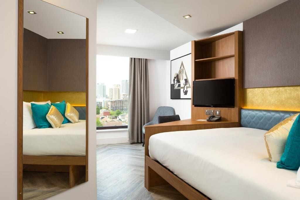 Ein Hotelzimmer mit Bett, Schreibtisch, Stuhl, Fernseher und Blick auf die Stadt.