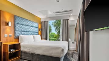 Habitación de hotel con una cama grande, una mesita de noche de madera, un televisor integrado y vistas al exterior.
