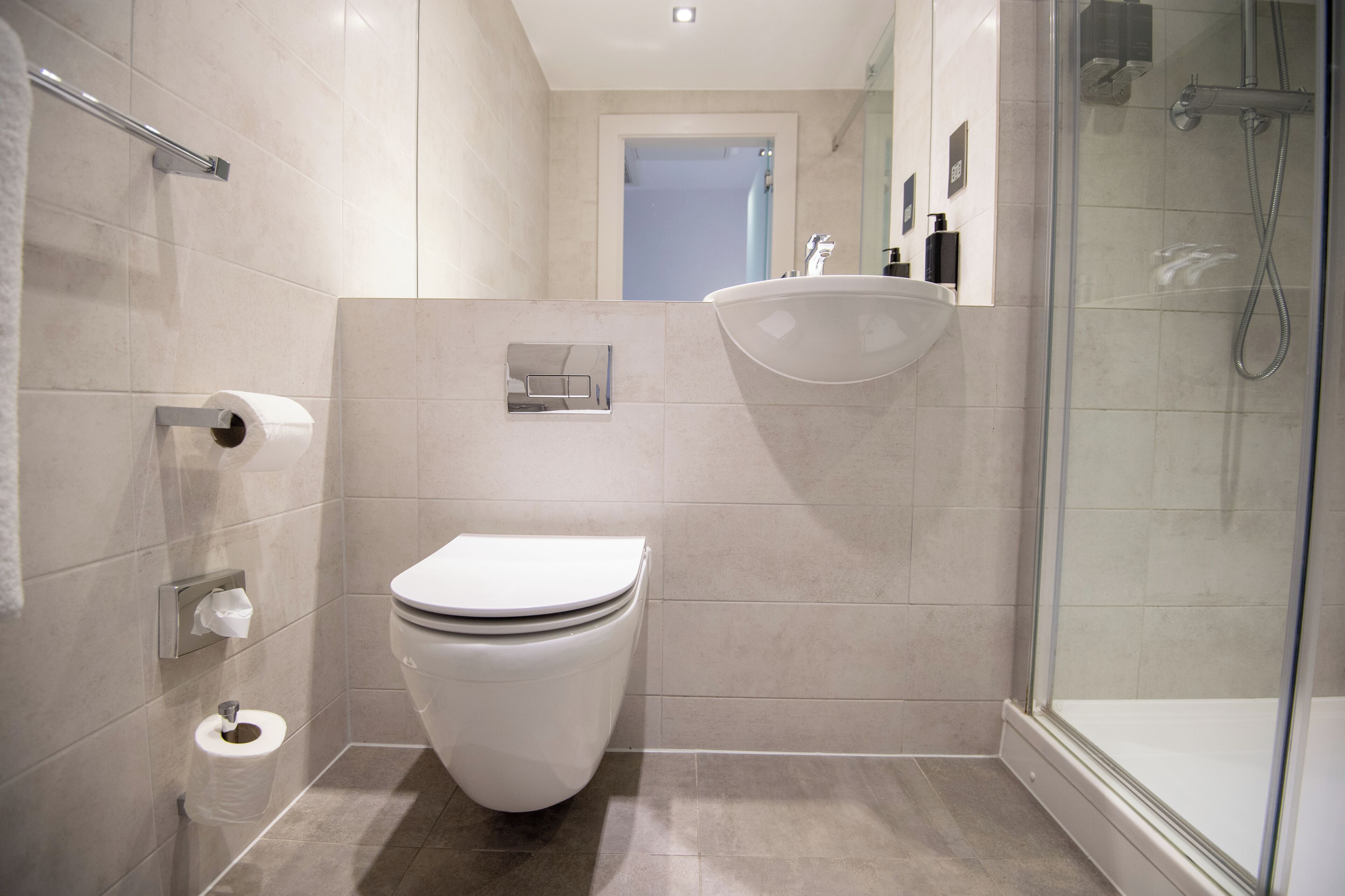 Egy modern fürőszoba, amelyben WC, mosdókagyló és zuhanyzó található.