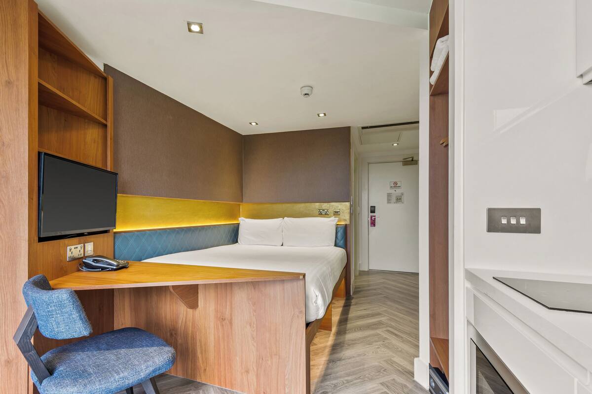 A hotel room with a bed, a desk with a chair, a television, and a wardrobe.