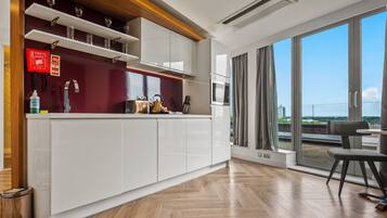 Eine moderne Küche mit weißen Schränken, einer Holzausziehtheke und Blick auf die Stadt durch große Fenster.