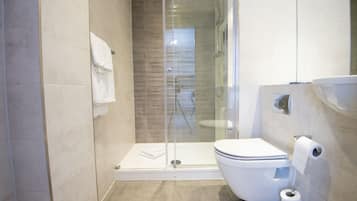 A modern bathroom with a glass-enclosed shower, a toilet, and a sink.