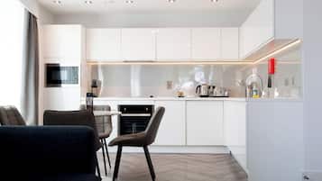 A modern kitchen with white cabinetry, a built-in oven, and a dining area with a table and chairs.
