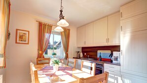 A kitchen with white cabinets, a wooden table, and a hanging light fixture. - Ferienpark Am Meer Katamaran 1 (Butjadingen)