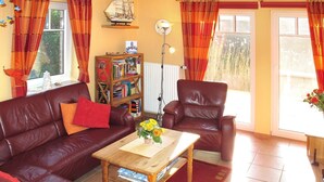 A cozy living room with a leather sofa, a wooden coffee table, a bookshelf, and a red armchair. - Ferienpark Am Meer Katamaran 1 (Butjadingen)