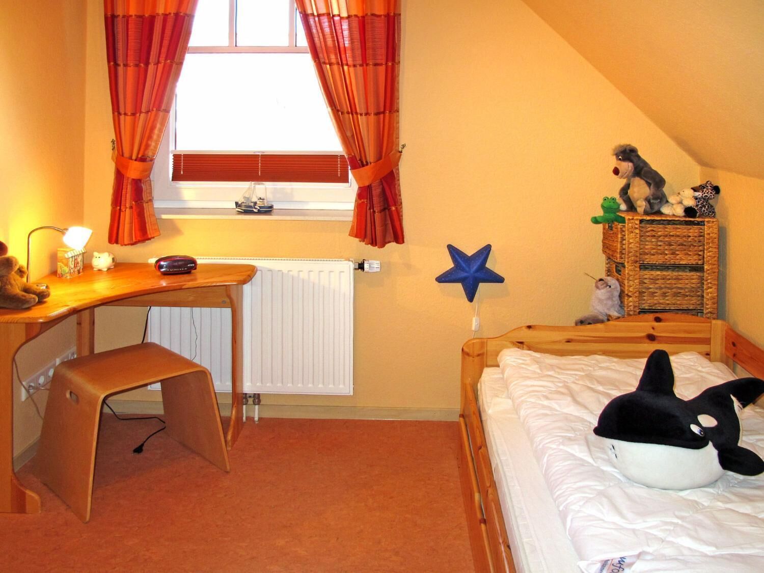 Un dormitorio con escritorio, cama, radiador, ventana con cortinas y decoración con estrellas.