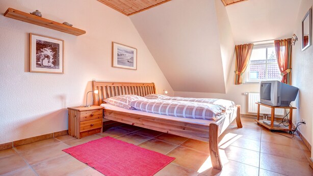 Une chambre à coucher avec un lit en bois, une table de chevet, un téléviseur posé sur un meuble et deux tableaux encadrés accrochés au mur.
