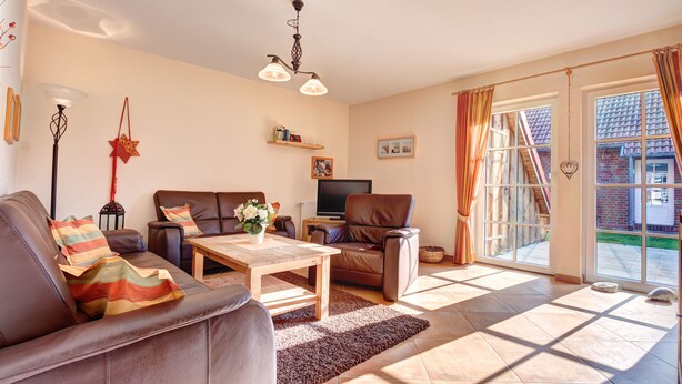 A living room with a sofa, a coffee table, a TV, and a fireplace. There is a window with curtains and a view of the outside. - Ferienpark Am Meer Katamaran 1 (Butjadingen)