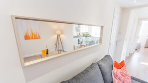 Un salon moderne avec un canapé gris, un grand miroir et une petite table sur laquelle se trouvent une bouteille et des verres.