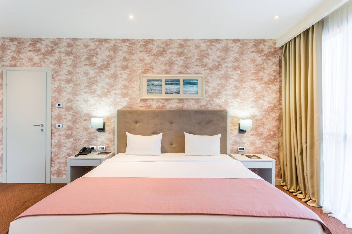 Habitación de hotel con cama, mesitas de noche, una puerta y un cuadro colgado en la pared.