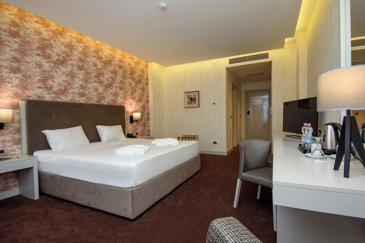 Una habitación de hotel con una cama grande, un escritorio con computadora, una silla y un televisor.