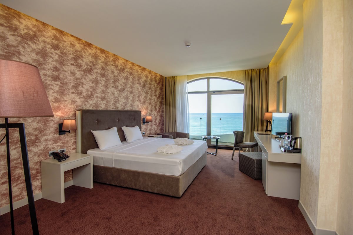 Habitación de hotel con una cama grande, un escritorio, una silla, una lámpara y vistas al mar.