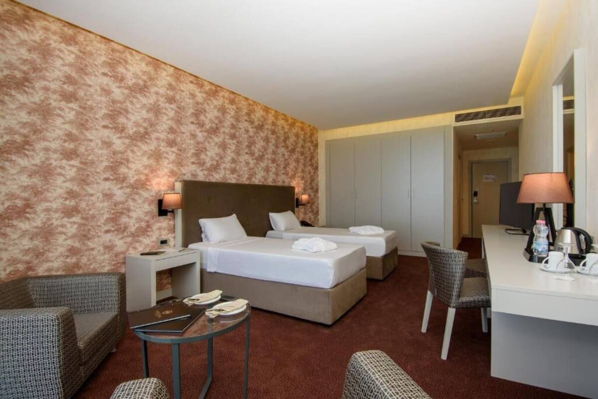 Habitación de hotel con dos camas, un escritorio, una silla, una mesita y un sofá.