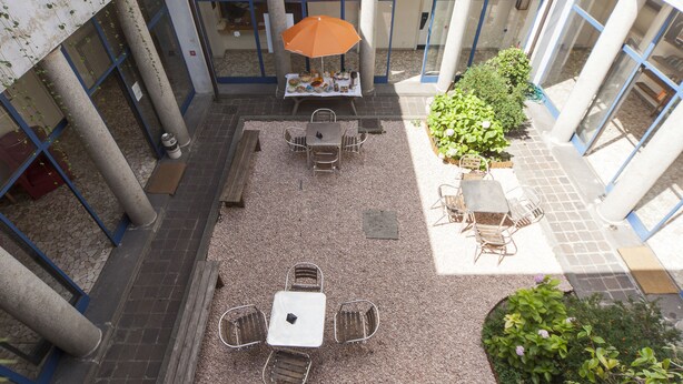 Un espacio al aire libre con patio, una mesa y sillas, una sombrilla y un pequeño jardín.