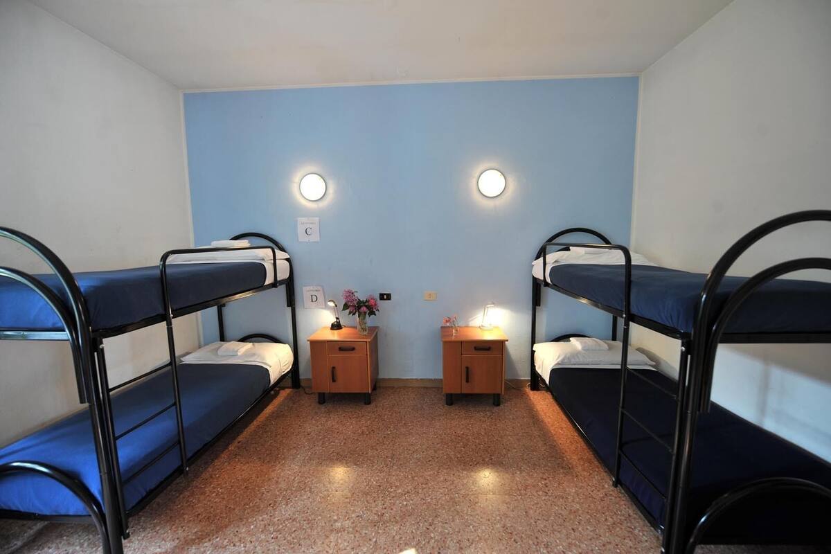 Un dormitorio con literas, dos mesitas de noche con lámparas y un escritorio pequeño con una silla.