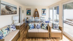 A cozy living room with a wicker sofa, a dining table, and a large window. - Beachside Apartment On The Beach (Totland Bay)