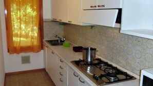 A compact kitchen with white cabinets, a gas stove, a microwave, and a window with orange curtains.