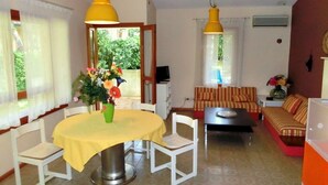 A dining area with a yellow table and chairs, a flower vase, and a sofa in the background.