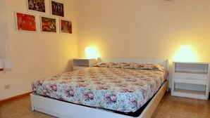 A bedroom with a floral bedspread, two bedside tables, and a wall with framed pictures.