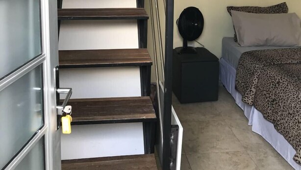 Una escalera de madera con barandillas de metal que lleva a un dormitorio con una cama y una mesita de noche.
