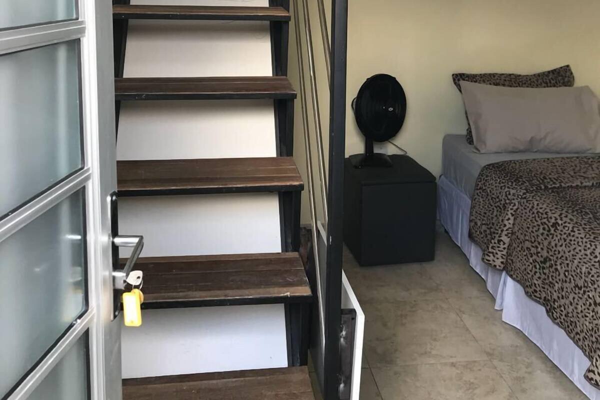 Un escalier avec des marches en bois et des rampes en métal menant à une chambre à coucher équipée d’un lit et d’une petite table de chevet.