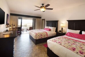A hotel room with two beds, a desk, a ceiling fan, and a balcony with a view.