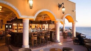 An outdoor bar area with multiple seating arrangements, including bar stools and tables, and a view of the ocean. - Confortable Family Suite 2BD at Cabo San Lucas (Cabo San Lucas)