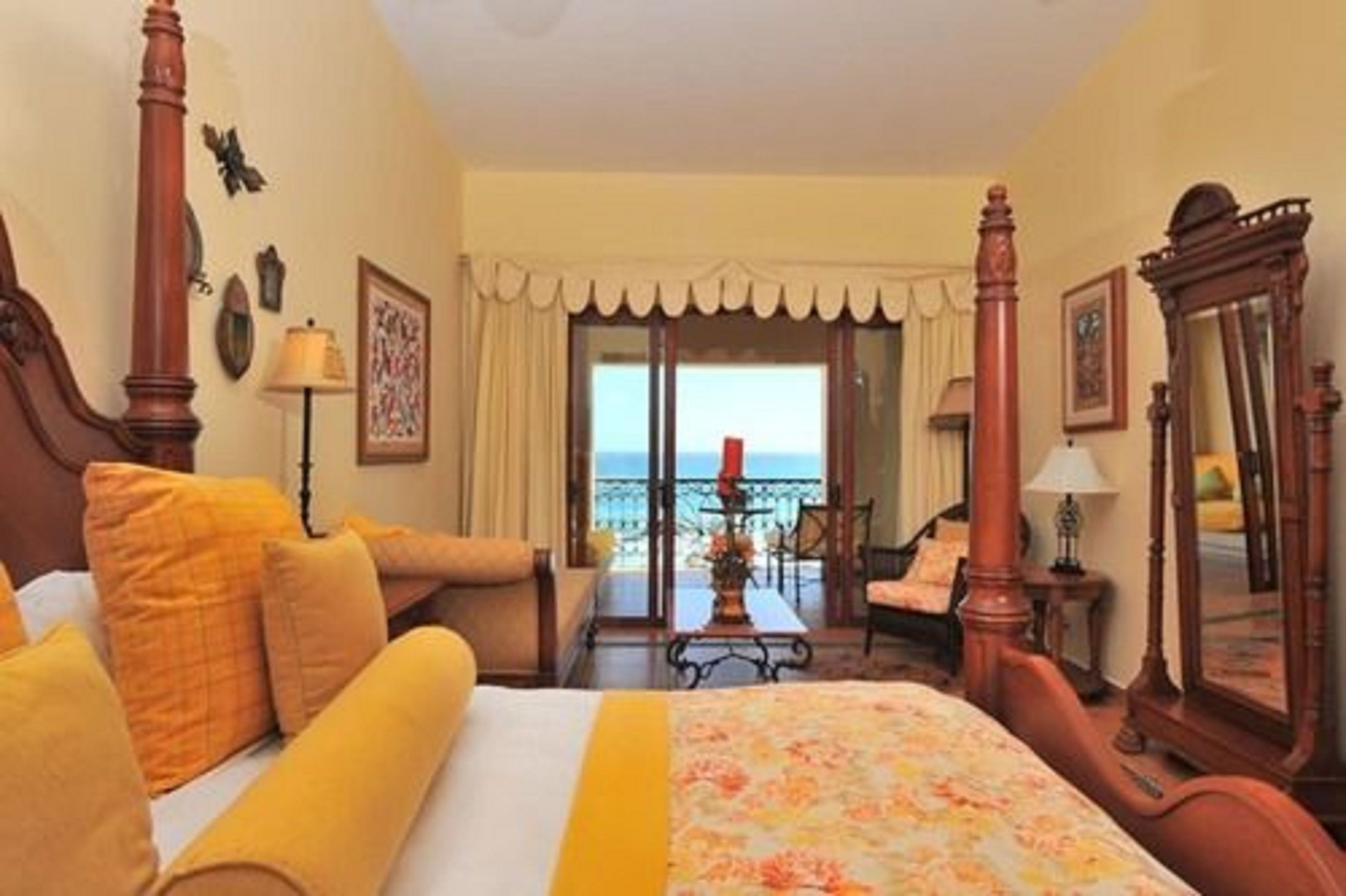 Habitación de hotel con una cama grande, un área de descanso y vistas al mar, además de un balcón con barandilla.