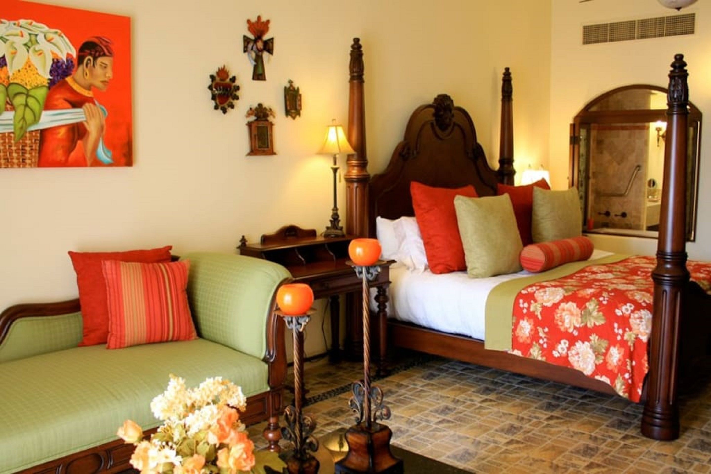 Una habitación tradicional con cama, sofá verde, mesita de noche y lámpara.