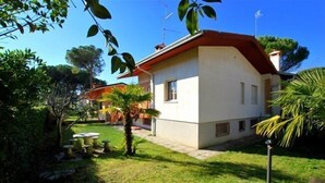 A single-story house with a red roof and white walls, surrounded by a well-maintained garden with various plants and a small patio area. - Villa a Lignano Riviera with air conditioning (Lignano Sabbiadoro)