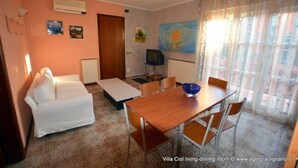 A living-dining room with a sofa, a wooden dining table, and a TV. - Villa a Lignano Riviera with air conditioning (Lignano Sabbiadoro)