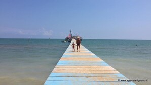 A wooden pier extending into calm sea waters, with a small boat docked at the end. - Villa a Lignano Riviera with air conditioning (Lignano Sabbiadoro)