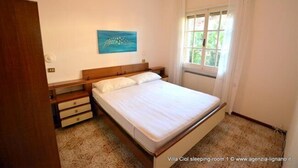 A bedroom with a wooden bed, a nightstand, a dresser, and a window with curtains. - Villa a Lignano Riviera with air conditioning (Lignano Sabbiadoro)