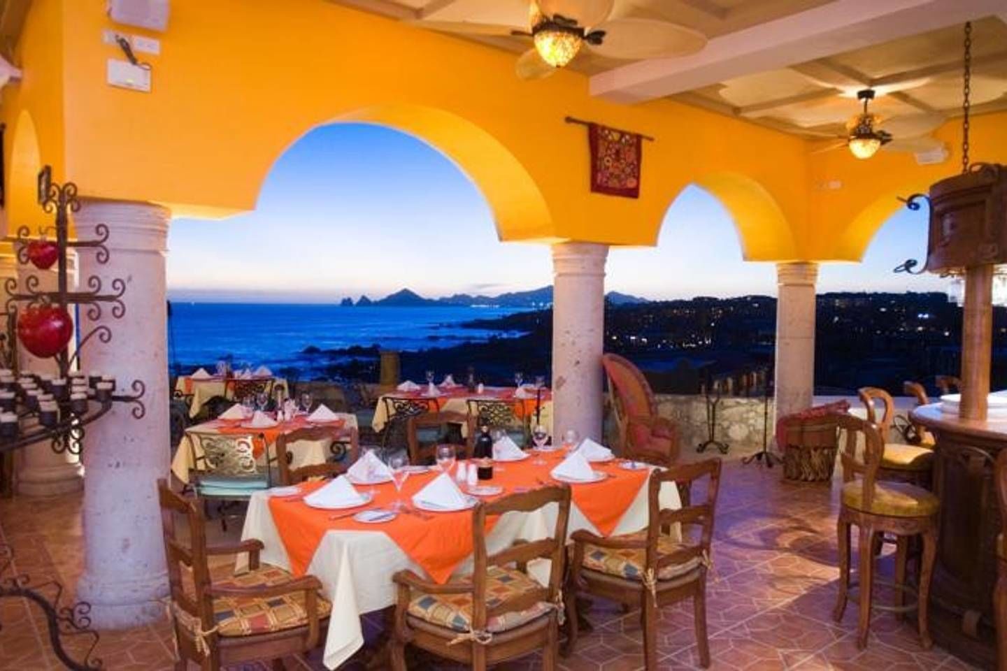 Ein Restaurant mit gedeckten Tischen, Blick auf das Meer und eine Küstenstadt im Hintergrund.