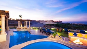 Ein Poolbereich mit zwei Pools, Sitzgelegenheiten im Freien und Blick auf das Meer im Abenddämmerung.