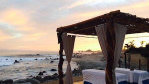 Ein Strandbett mit Holzbaldachin und weißer Bettwäsche mit Blick aufs Meer.