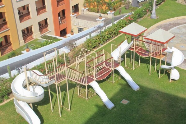 A playground with slides and climbing structures, surrounded by a well-maintained lawn and a building with balconies.