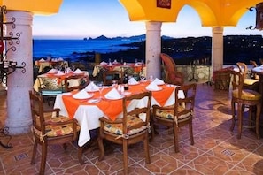 An outdoor dining area with tables set for two, featuring a coastal view at dusk.