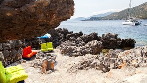 A rocky beach with a large rock formation, a sailboat in the background, and colorful outdoor seating. - Zidanos Luxurious Villa (Lefkada)