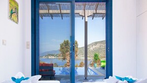 A room with two beds, a large sliding glass door leading to an outdoor area with a pool and a view of the landscape. - Zidanos Luxurious Villa (Lefkada)